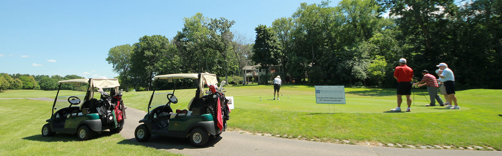 Image of four people playing golf on a golf course with two golf carts off to the side