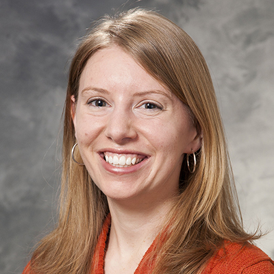 Smiling white woman with shoulder-length light brown hair. Wearing an orange top.