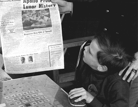 A black and white picture of a young boy looking at a newspaper