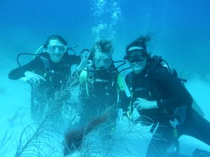 Two teenagers and an adult in full scuba diving gear posing for a picture underwater