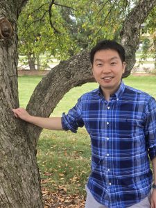 Man in a plaid shirt standing next to a tree