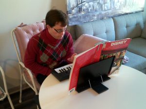 Man in red sweater playing a keyboard at a table