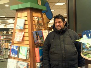 Man in a winter coat standing next to a book display