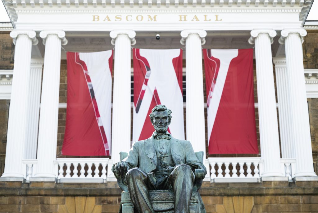 The Abraham Lincoln statue sits before Bascom Hall on Bascom Hill at the University of Wisconsin-Madison during spring on April 2, 2025. A three-paneled W banner hangs between the building’s columns. (Photo by Jeff Miller / UW–Madison)