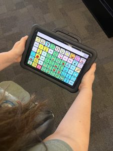Someone holding an AAC device displaying different picture icons on the screen