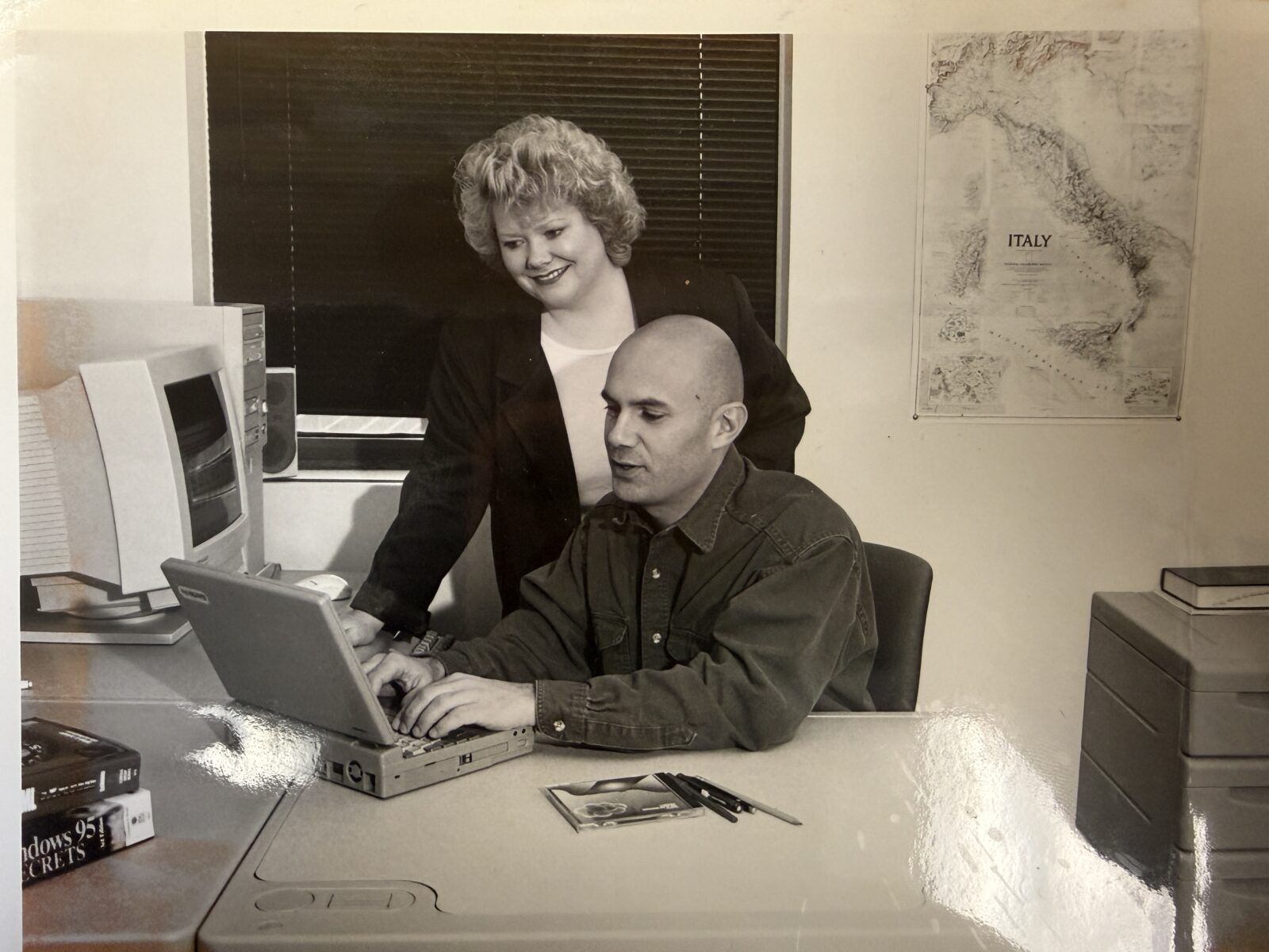 Black and white photo of Linda and Ernie looking at an old laptop inside of an office