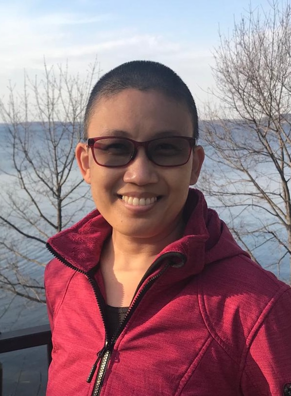 Jenn Soriano, wearing red glasses and a red sweater looking at the camera, with the lake behind her.