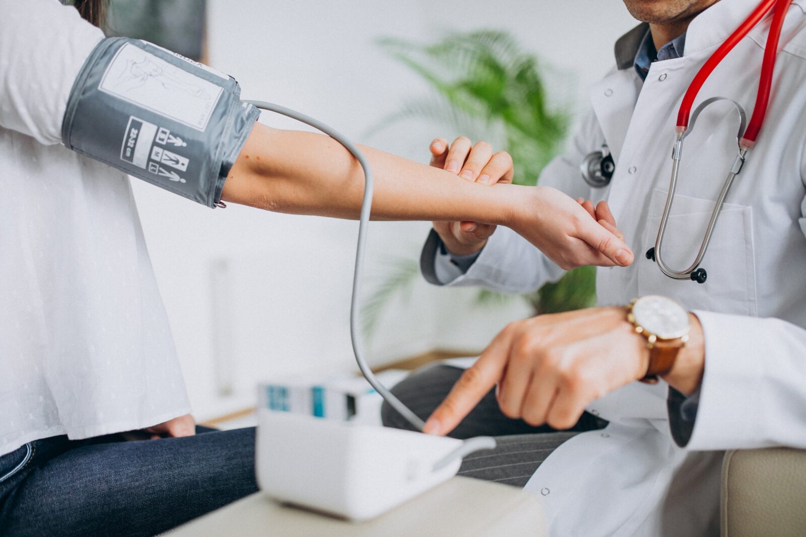 male medical doctor, wearing a white coat, taking blood pressure from a female patient using an automatic digital monitor